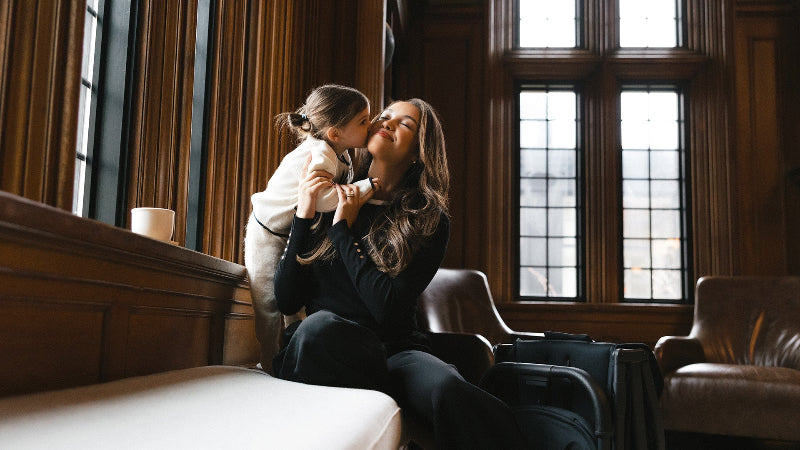Woman and child embracing in a room with wooden paneling and large windows.
