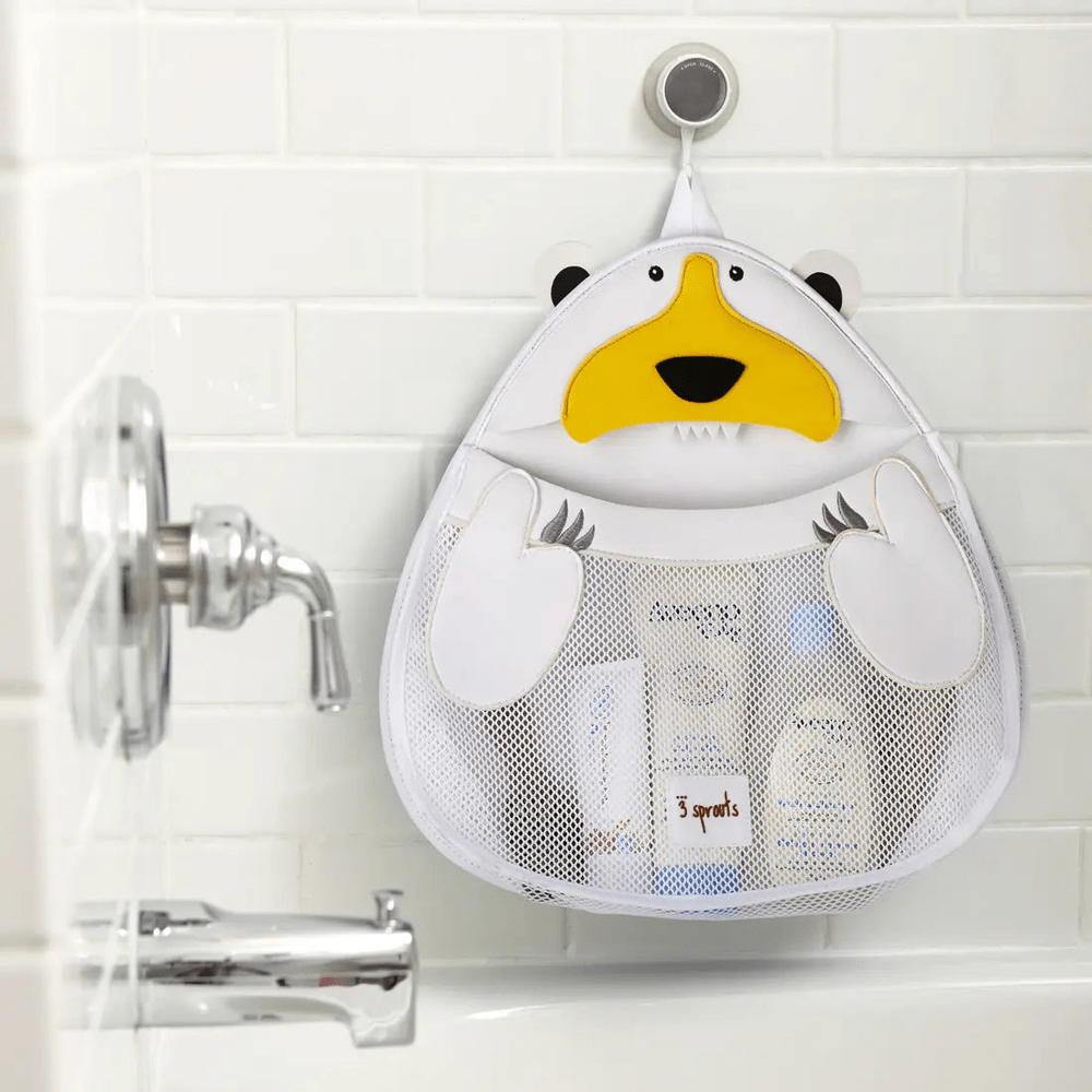 3 Sprouts Bath Storage bag in white mesh with yellow penguin face, hanging on a tile hook and holding toiletries.