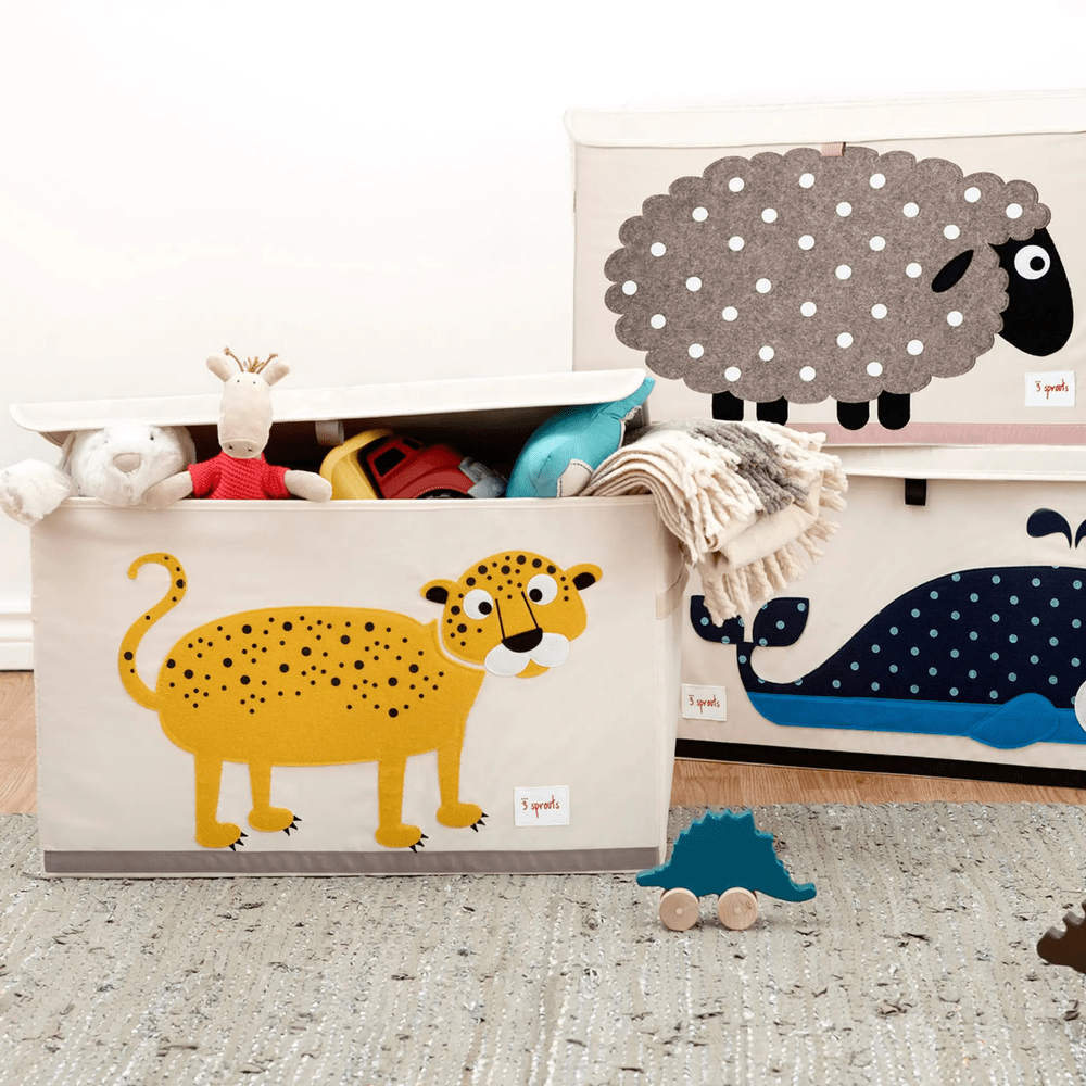 3 Sprouts Toy Chest in cream with a yellow leopard graphic, lid open revealing plush toys and blankets.