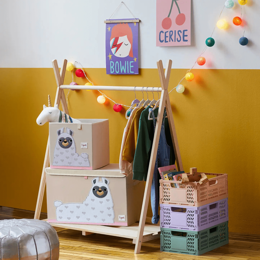 3 Sprouts Toy Chest with llama motif, plus matching pale pink boxes on a wooden rack in a cozy playroom.