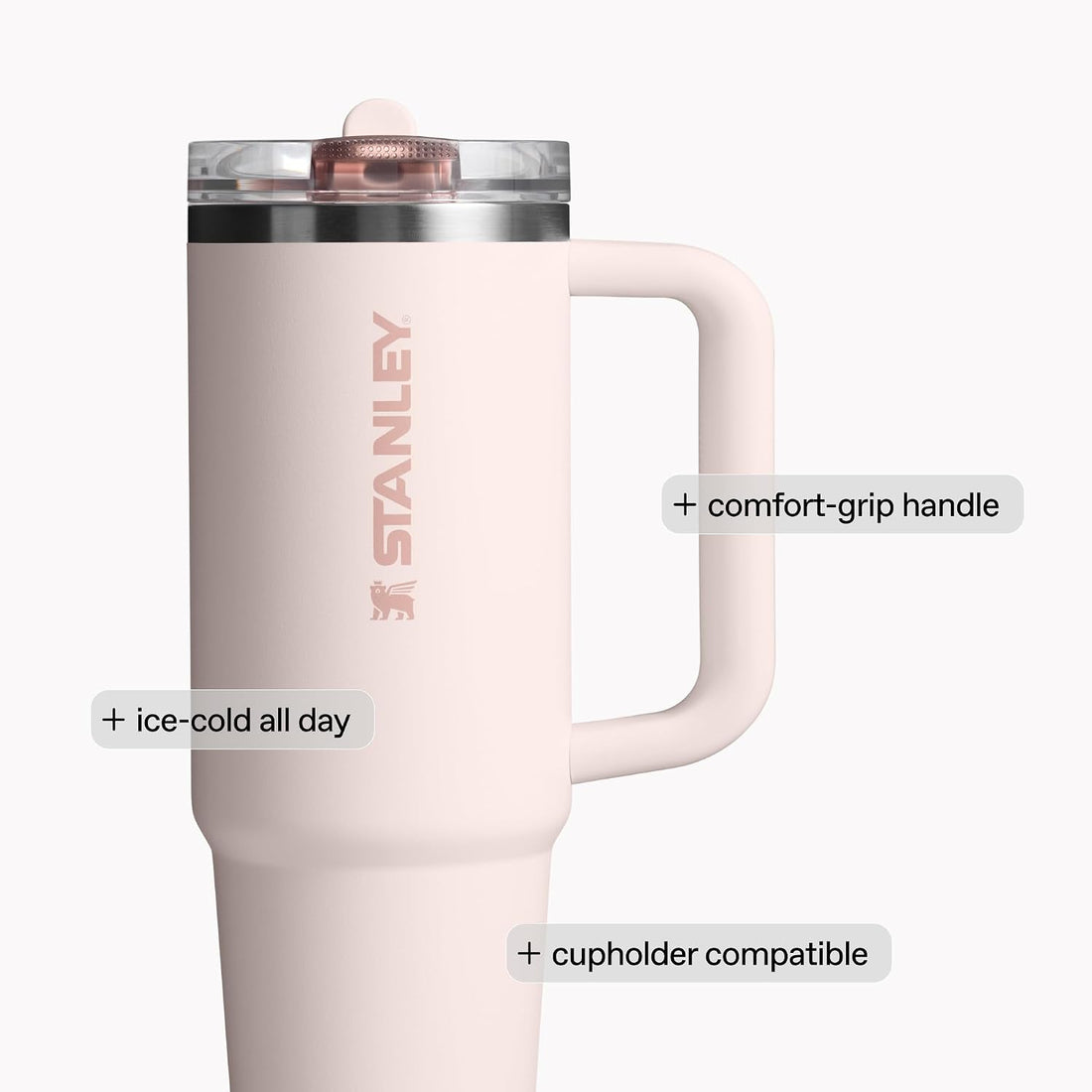 A pale pink Stanley travel tumbler with a handle, shown on a light gray background with feature callouts: 'comfort-grip handle', 'ice-cold all day', and 'cupholder compatible'.