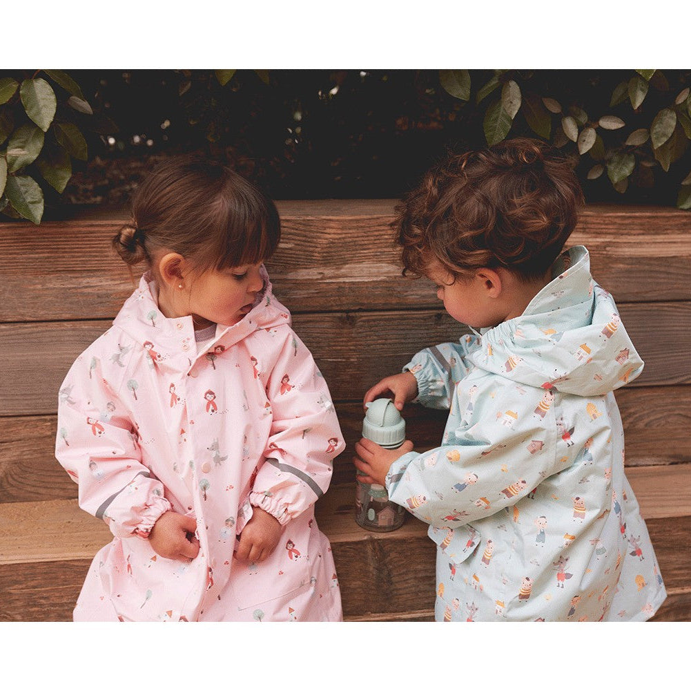 Two children in floral raincoats standing next to a wooden wall with greenery.