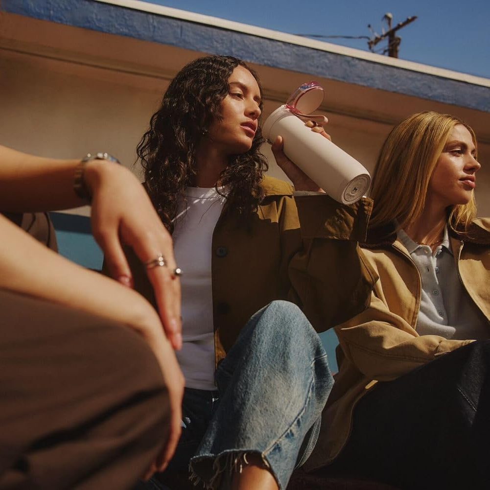 Two women sitting together, one holding a cup, on a sunny day.