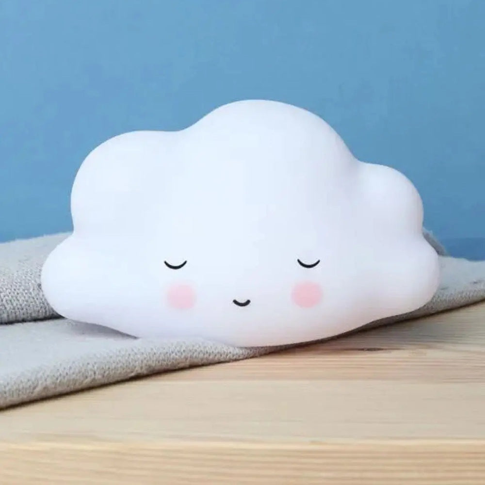 A Little Lovely Company Little Night Light cloud lamp glows softly with a sleepy face on a wooden bedside.