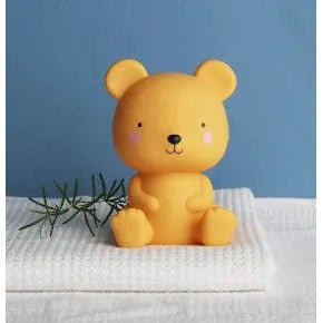 A Little Lovely Company Little Night Light bear sits on a white towel in a calm blue room, emitting a soft warm glow.