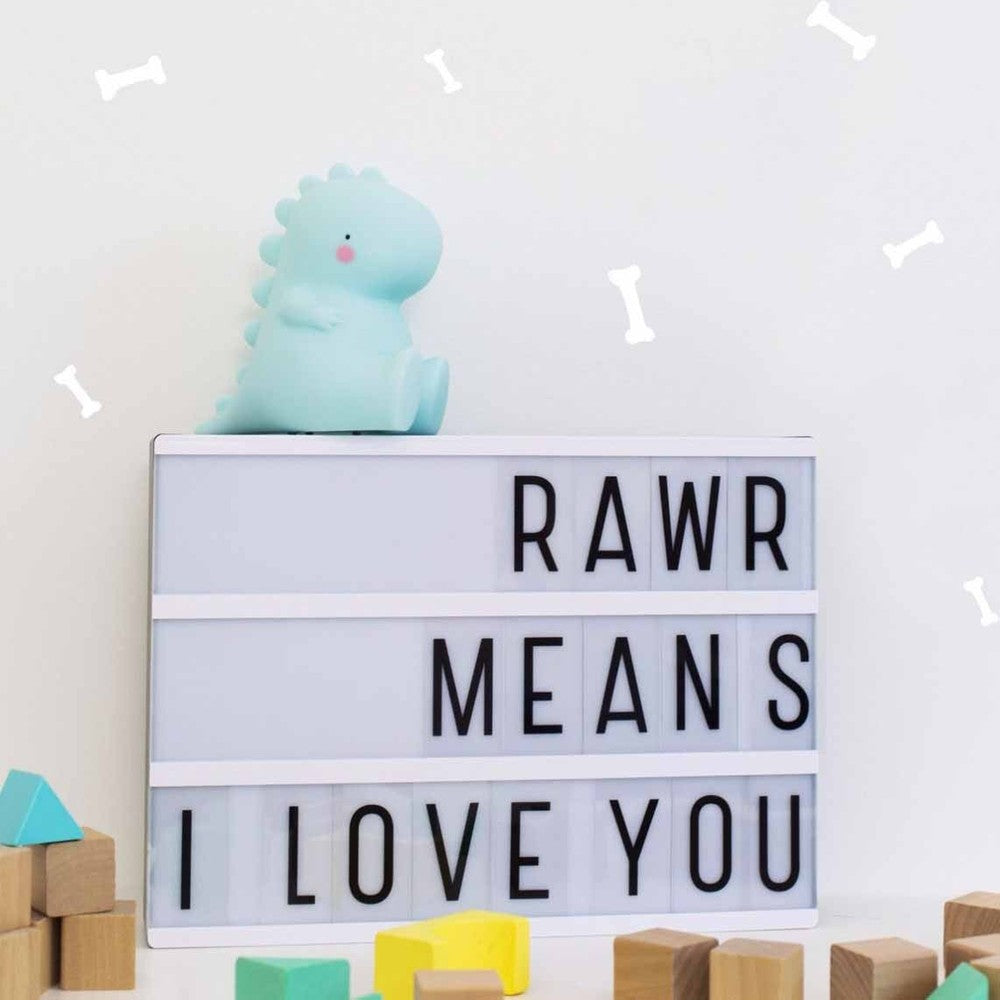 A Little Lovely Company Little Night Light T-Rex mint green perched on a white lightbox, creating warm ambiance with wooden blocks.