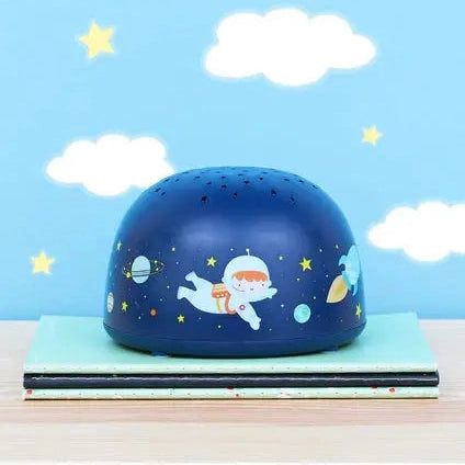 A Little Lovely Company Projector Night Light in a blue dome featuring an astronaut and planets, resting on books.