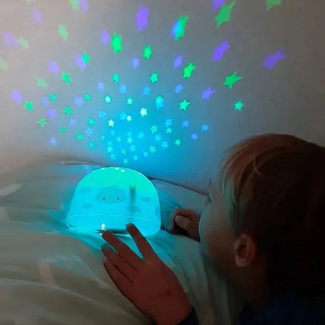 A Little Lovely Company Projector Night Light in blue casts blue-green starry patterns on the wall as a child lies in bed.