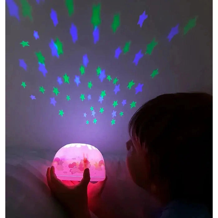 A Little Lovely Company Projector Night Light, pink base, held by a child projecting green and blue stars on the wall.