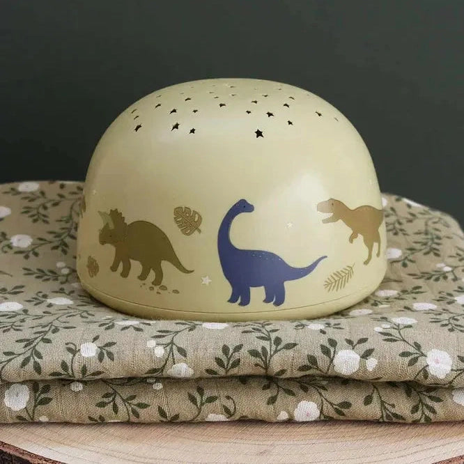 A Little Lovely Company projector night light, beige dome with dinosaur silhouettes and star cutouts, ready to project stars.