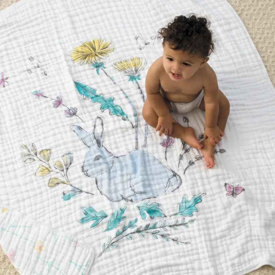 Aden+Anais Classic Dream Blanket; white quilt with blue bunny motif and floral accents as baby sits on it.