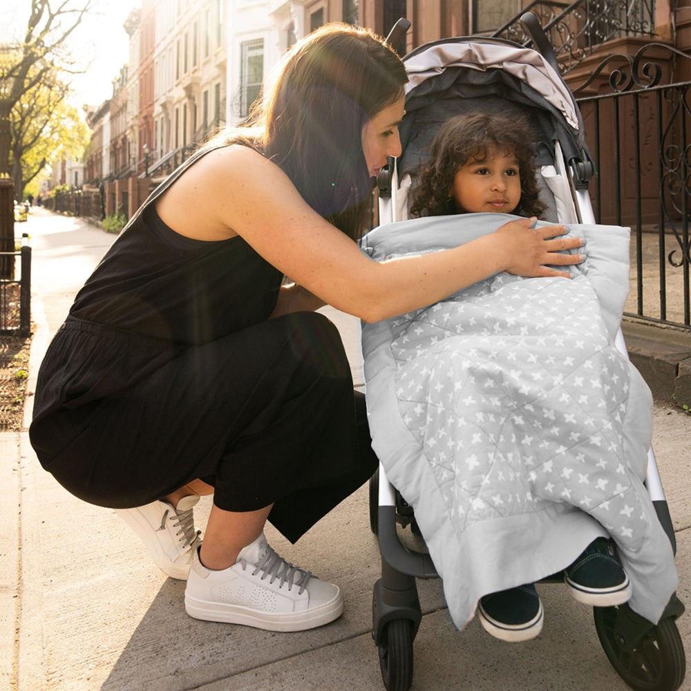 Aden+Anais Embrace Cross-Hatch weighted on-the-go blanket in gray draped over a stroller with a child