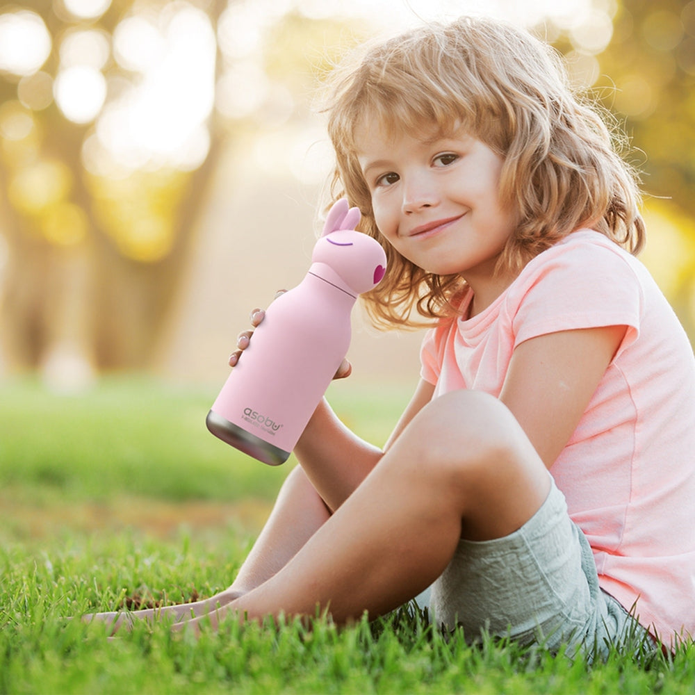 ASOBU Bestie Animal 16oz Bunny bottle, pink stainless steel, held by smiling girl outdoors on grass.