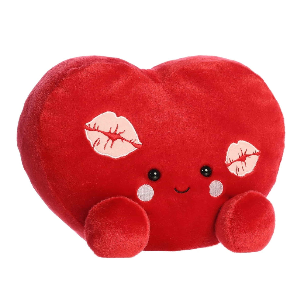 Red plush heart-shaped toy with black bead eyes, pink cheeks, stitched smile, kiss-print patches on sides.