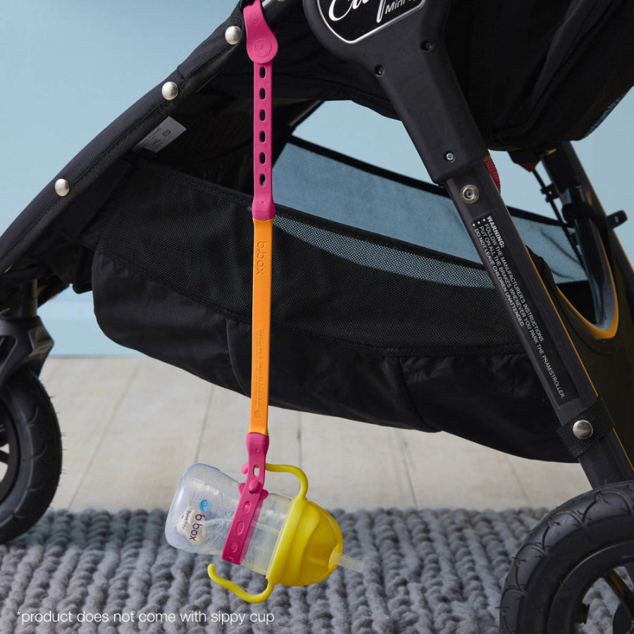 B.Box Connect A Cup sippy cup attached to a stroller with pink/orange strap and yellow lid