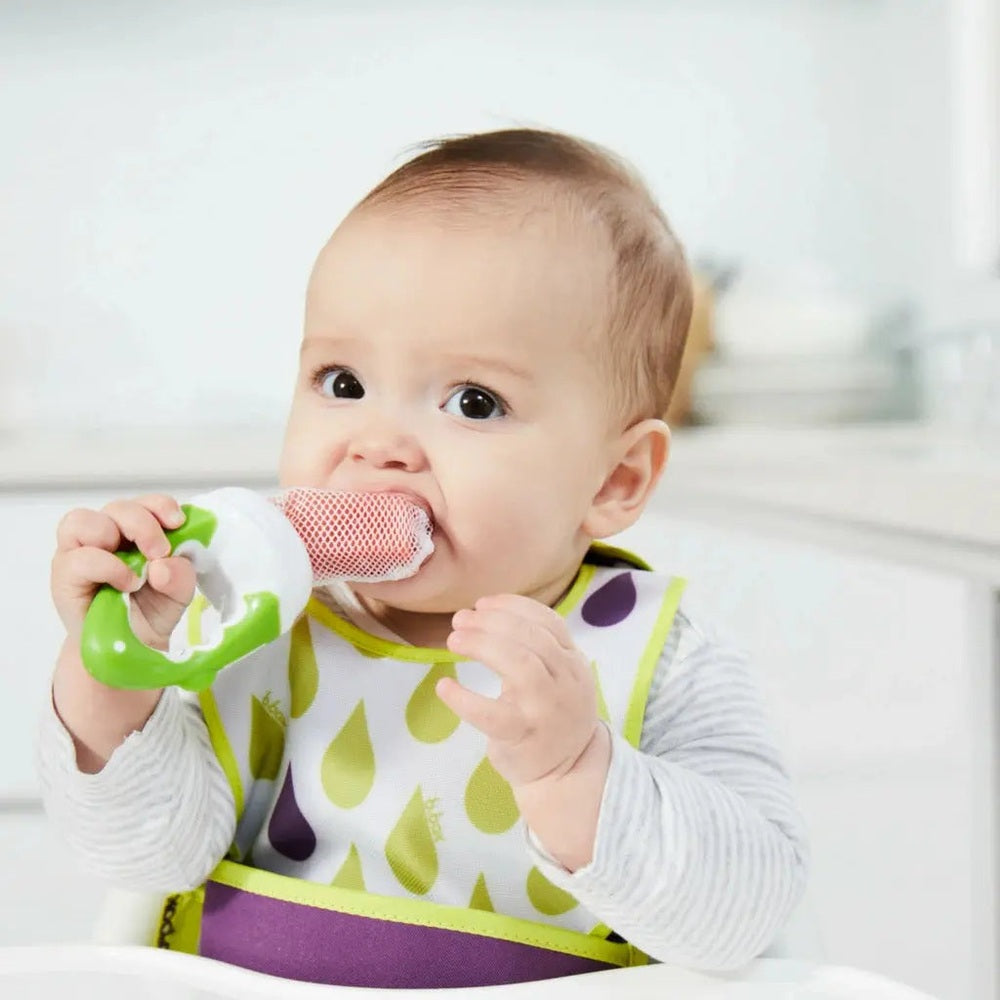 B.Box Fresh Food Feeder in green handle with pink mesh being chewed by a baby at mealtime