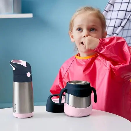 B.Box Insulated Food Jar set in pink and stainless steel on table as a child nearby shows its kid-friendly design.