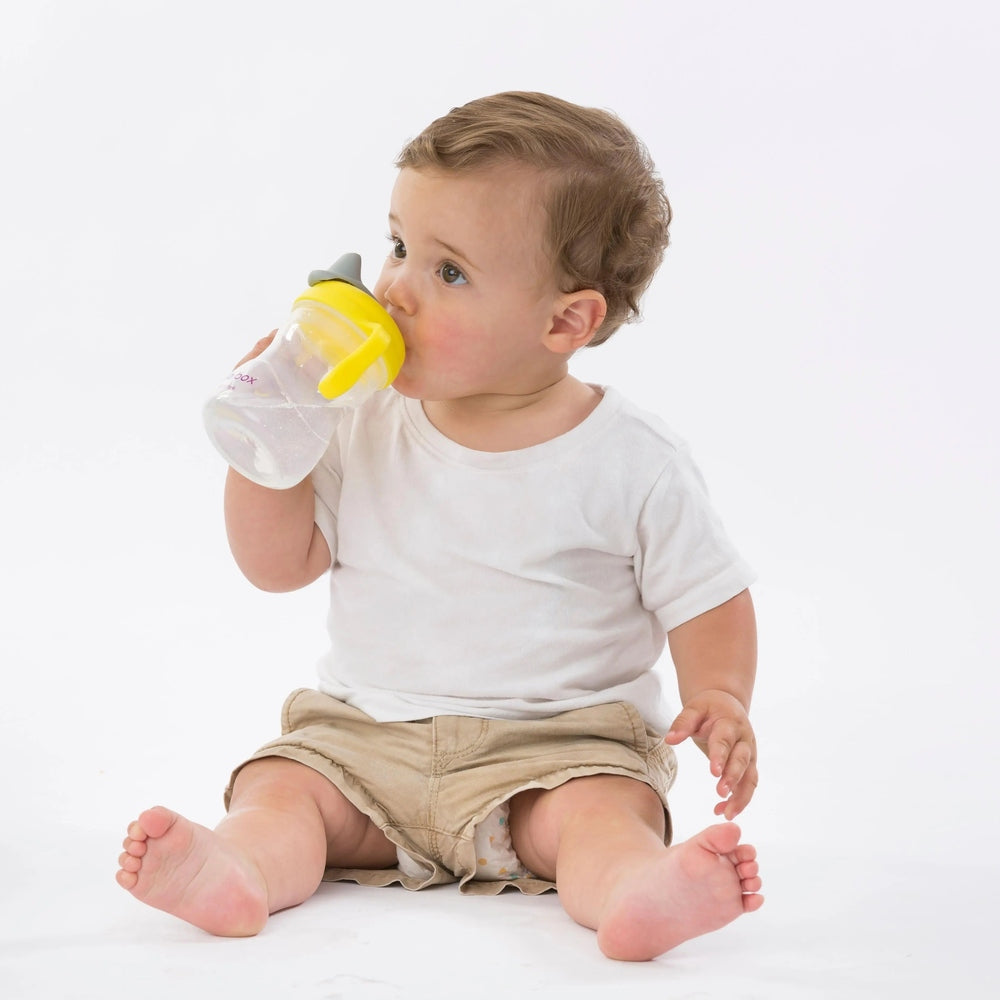 B.Box Spout Cup, clear bottle with yellow spout lid, as a seated baby drinks from it.