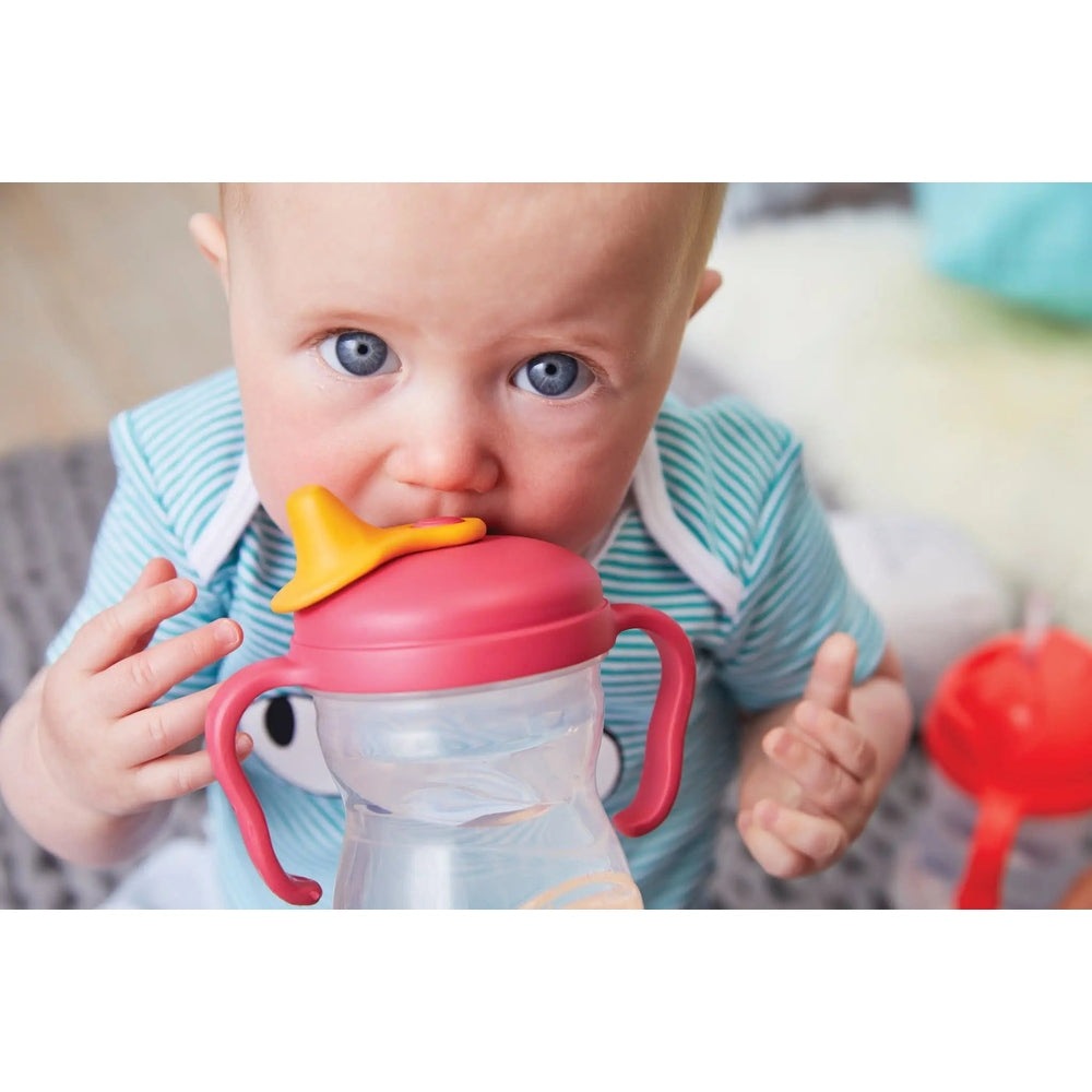 B.Box Spout Cup for babies with pink lid, yellow spout, and red handles, held by a baby.