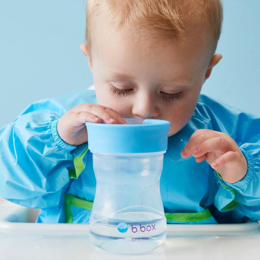 B.Box Training Cup in blue with wide lid; BPA-free, toddler sips water from it.