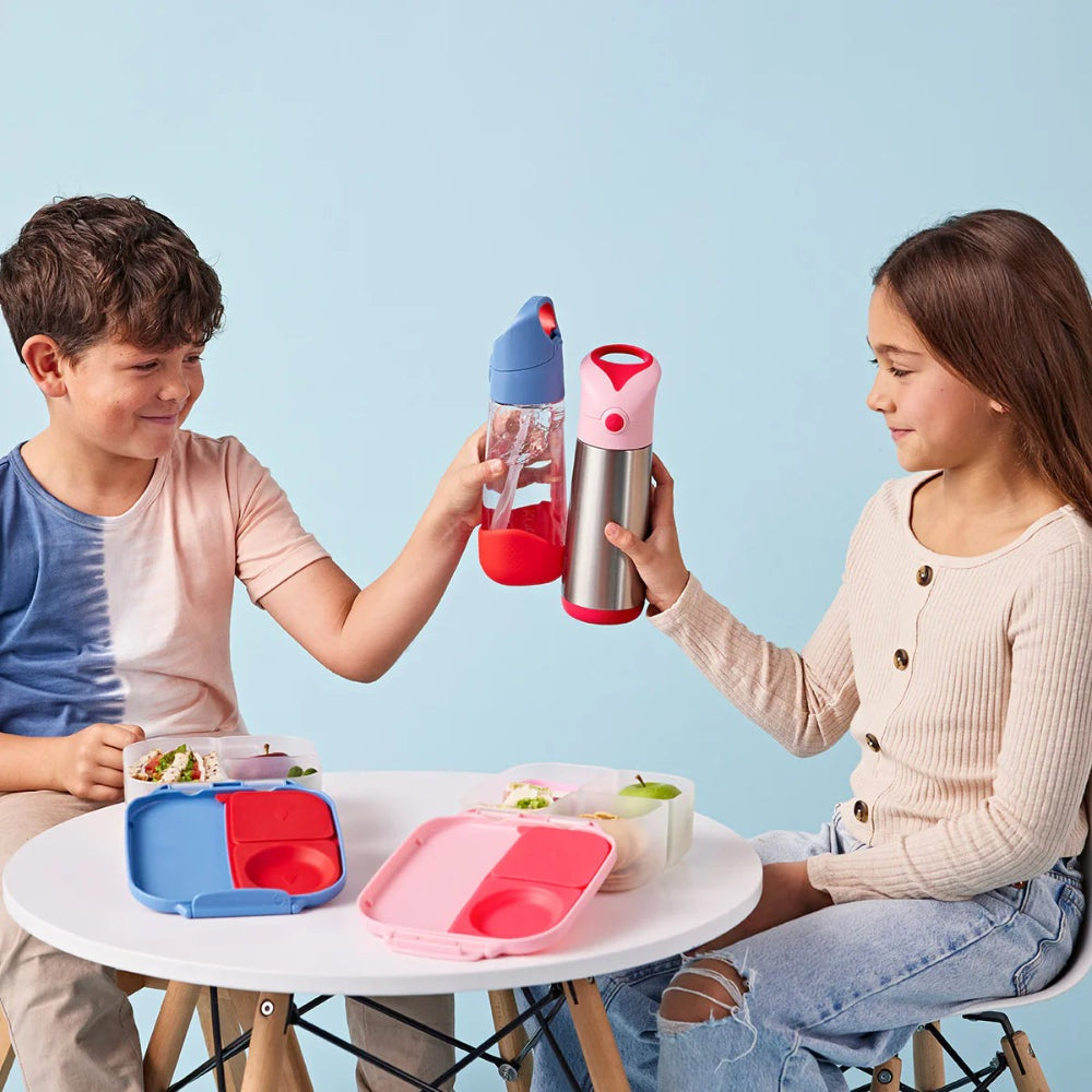 B.Box Tritan Drink Bottle 600 ml clinking between two kids, blue and pink lids, lunch boxes on table.