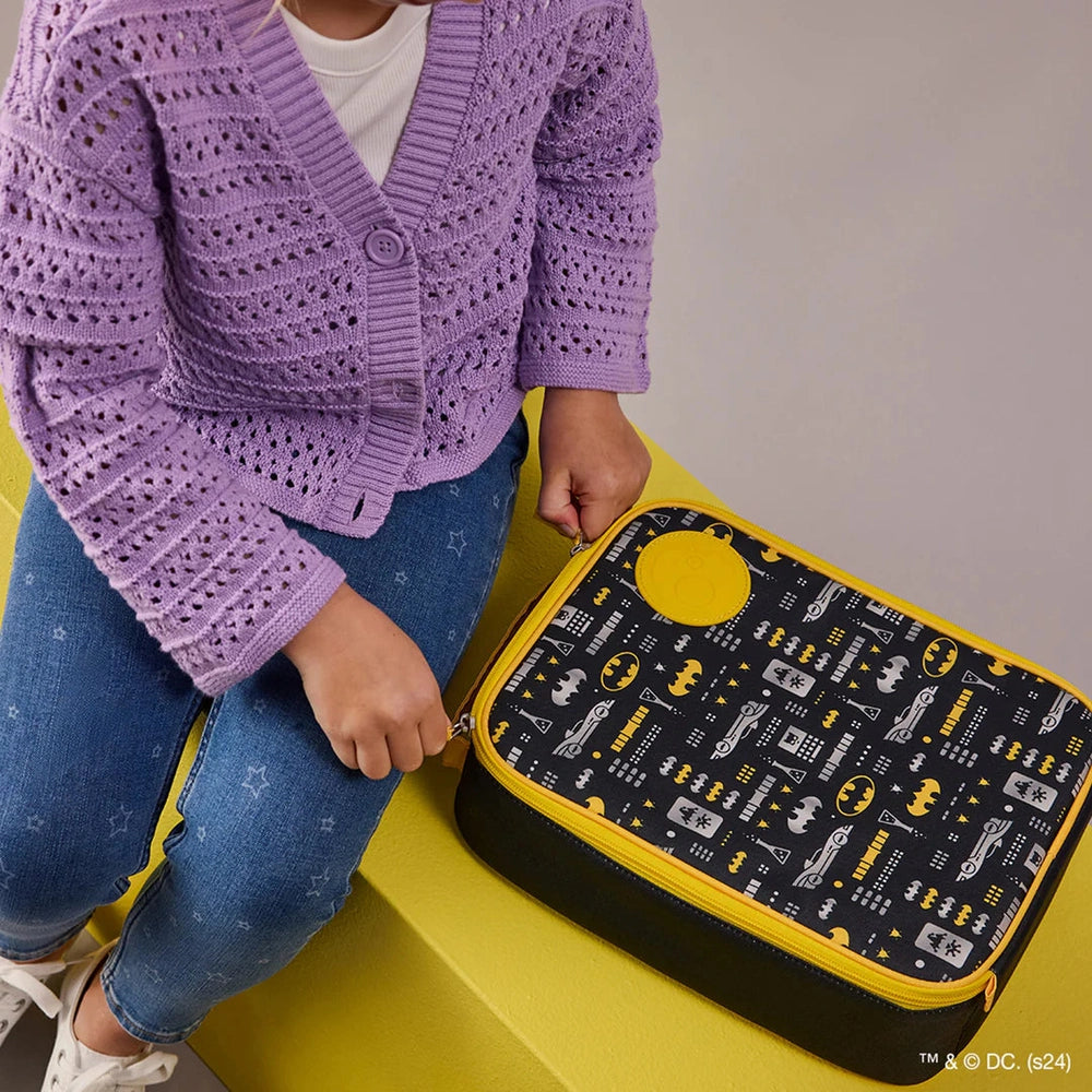 B.box Insulated Flexi Lunchbag with Batman pattern and yellow trim, carried by a child in a purple cardigan.