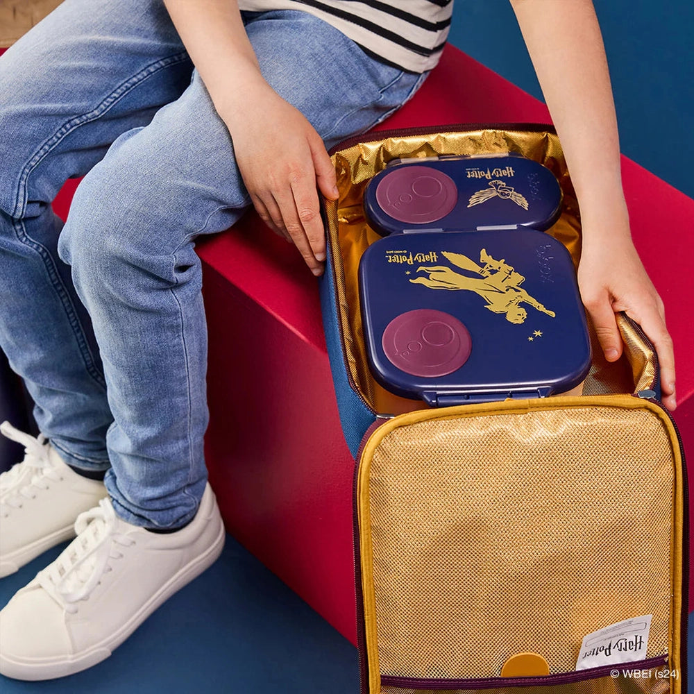 Child sits with a blue B.BOX Insulated Flexi Lunchbag, showing gold foil lining and purple compartments.