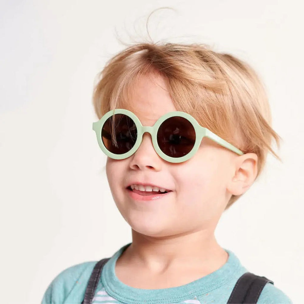 Kids sunglasses Babiators Euro Round All The Rage Sage with mint-green frames and dark lenses, worn by a smiling child.
