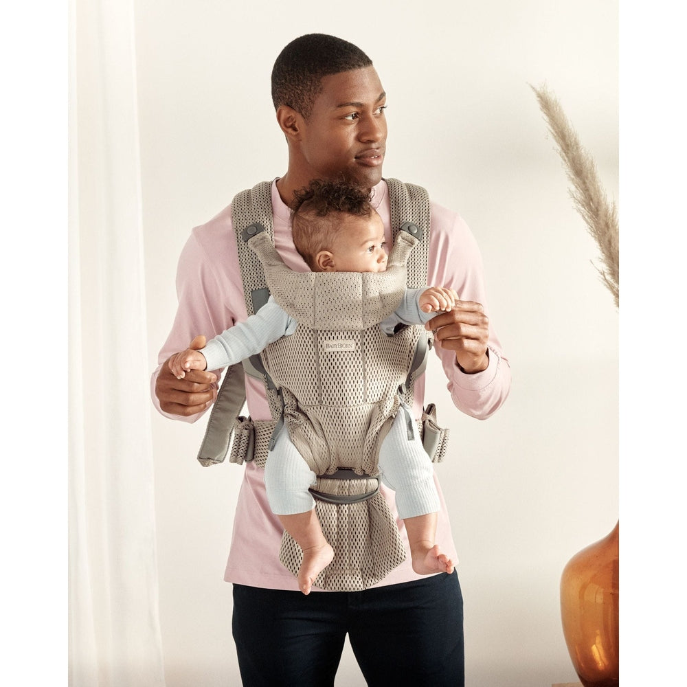 BabyBjörn Baby Carrier Free in beige worn by dad, with baby snug inside and straps securely fastened.