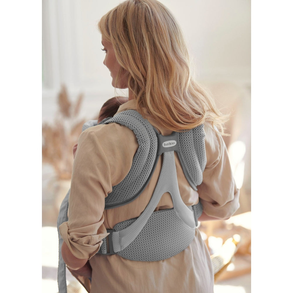 BABY BJÖRN Baby Carrier Free in gray worn by a mother with a baby on her back, showing breathable mesh straps and ergonomic support.