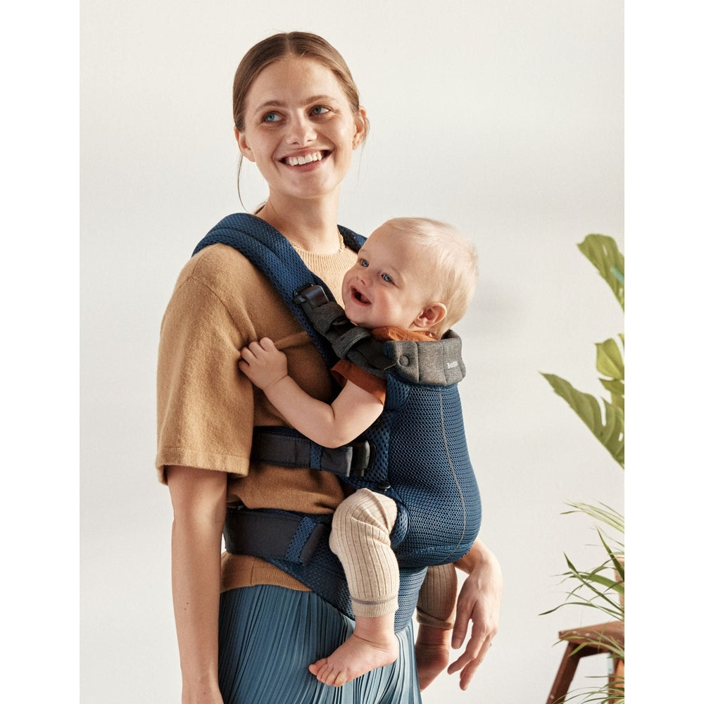 BabyBjörn Baby Carrier Free in navy blue mesh worn by a smiling mom with baby securely seated and strapped.