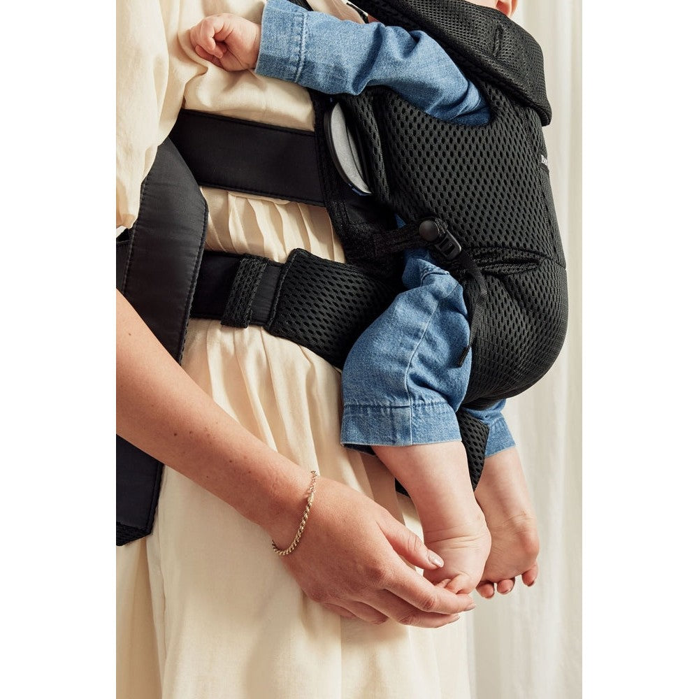 Baby Björn Baby Carrier Free in black mesh worn by a parent, with secure waist belt; caregiver supports a baby inside.