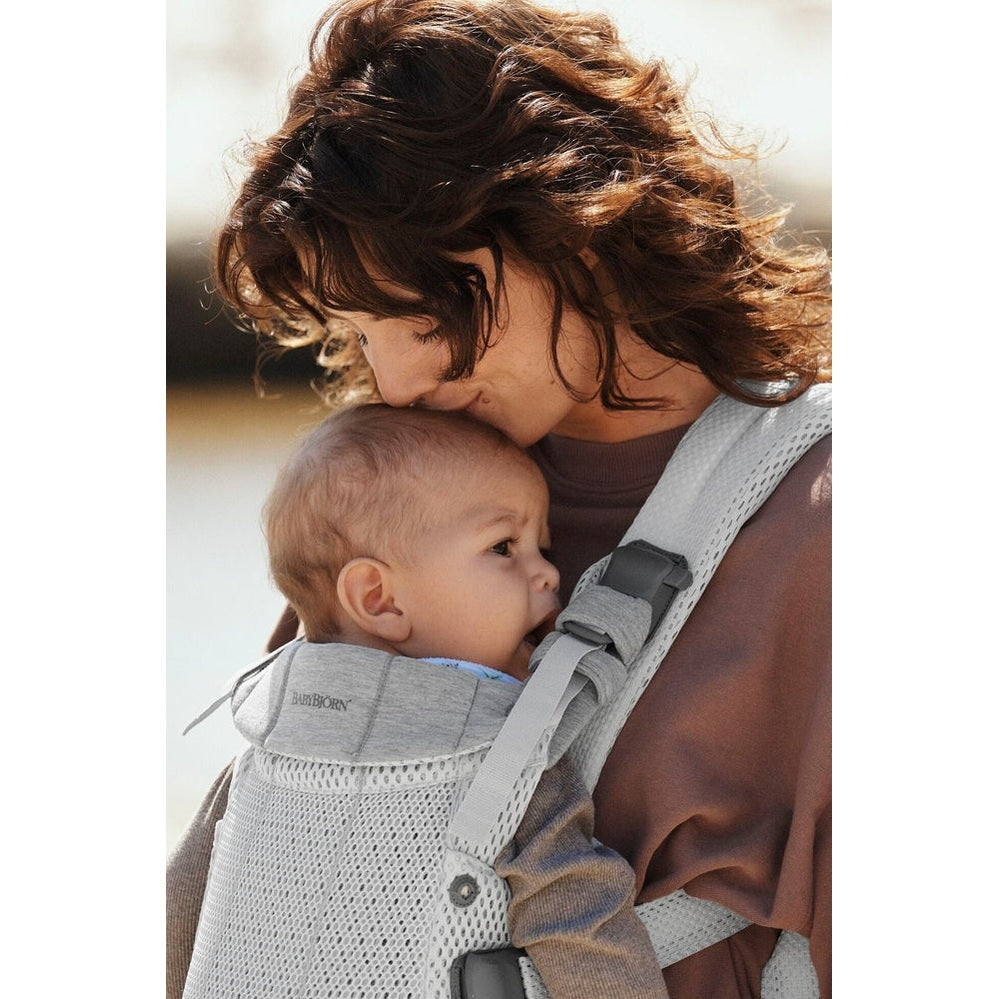 BabyBjörn Baby Carrier Harmony in gray worn by a mother as she hugs her baby chest-to-chest with secure straps.