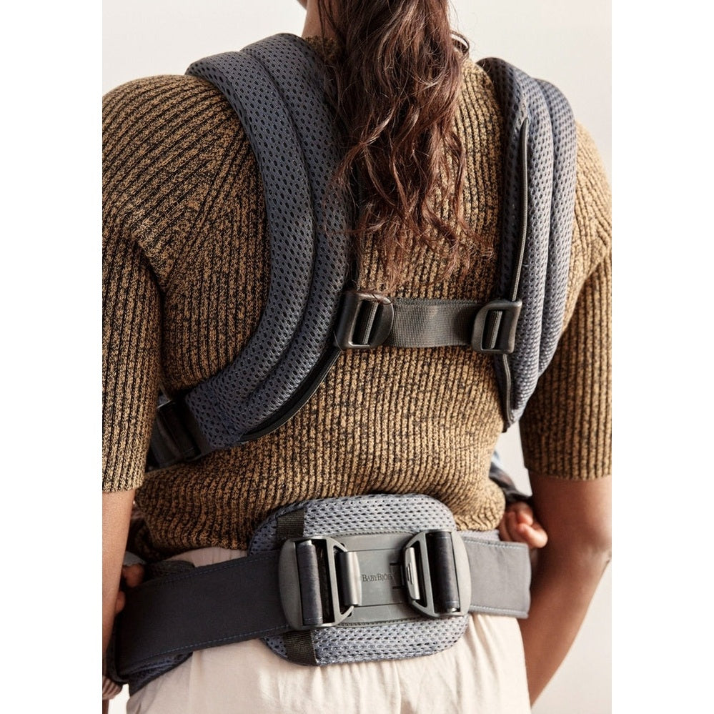 BabyBjörn Harmony baby carrier worn by adult, gray mesh straps and padded waist belt buckled.