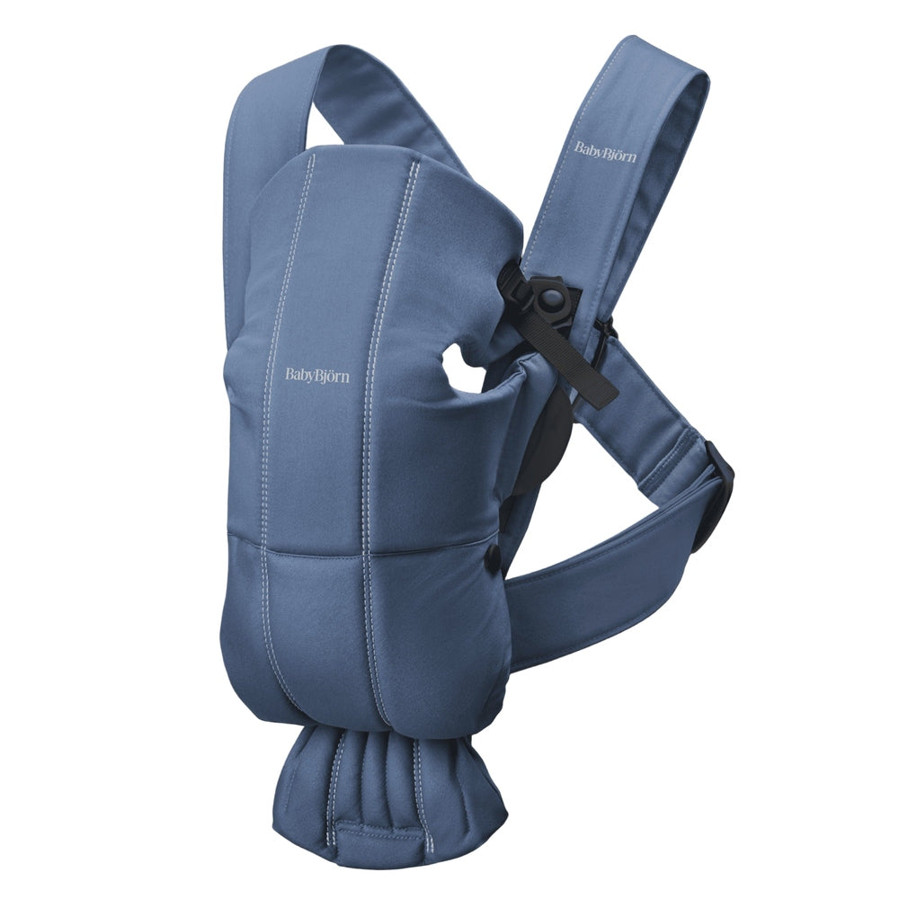 BabyBjörn Baby Carrier Mini in blue, ergonomic padded carrier worn by a caregiver with adjustable straps and waist belt.