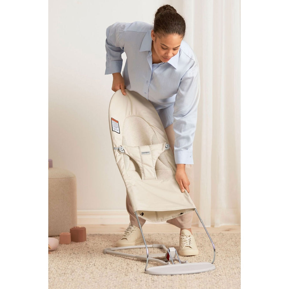 BabyBjörn Bouncer Bliss beige being assembled by a person, showing its lightweight frame and soft mesh seat.