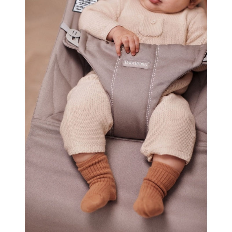 BabyBjörn Bouncer Bliss in gray, with a baby in cream knitwear and brown socks securely seated.