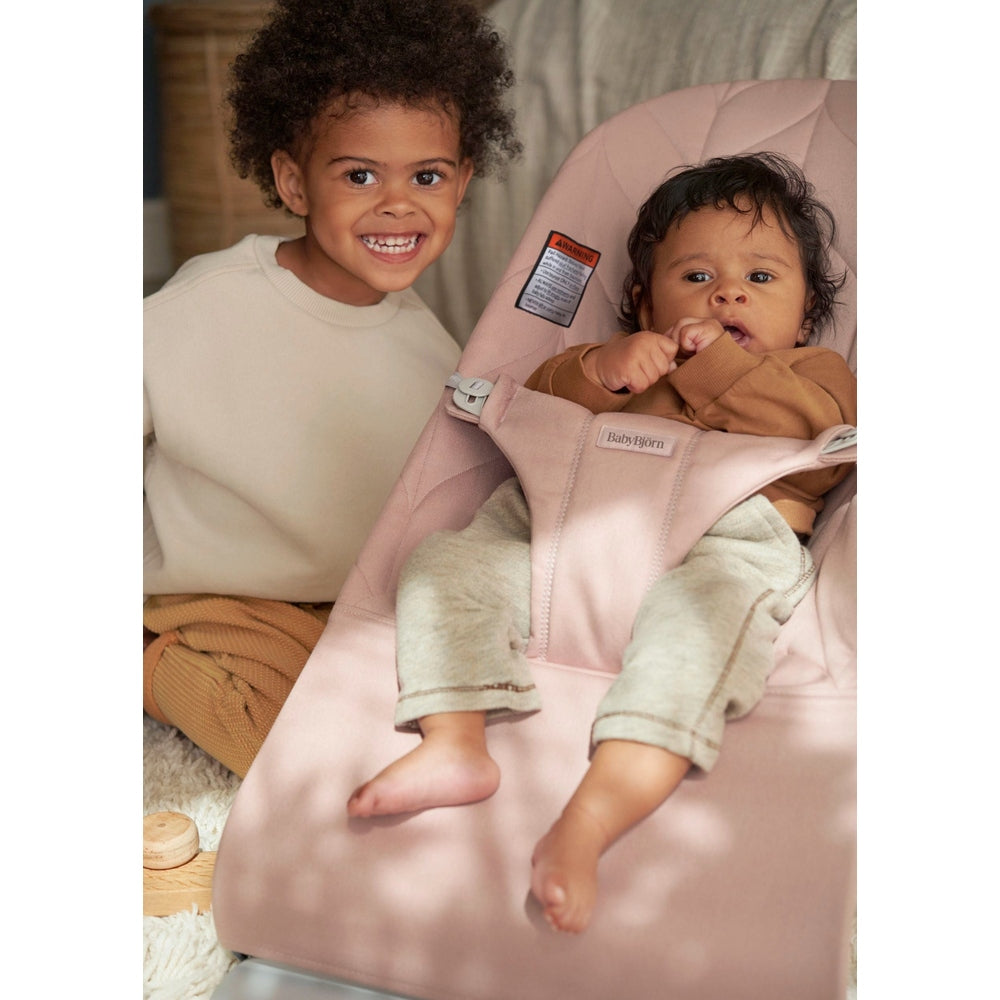 BabyBjörn Bouncer Bliss pink; a joyful sibling moment with baby securely buckled in the cozy bouncer.