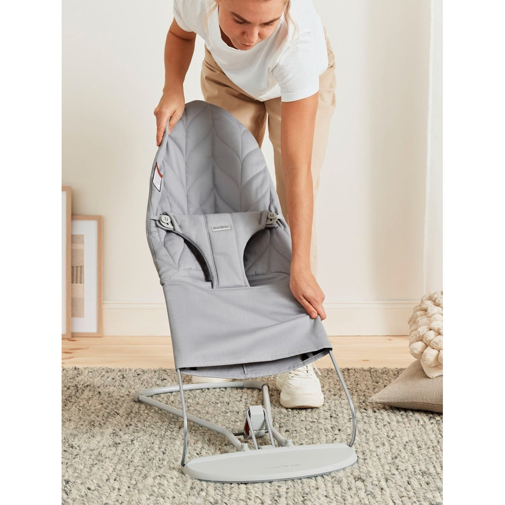 BabyBjörn Bouncer Bliss in gray, showing quilted seat and stable stand as a caregiver helps set it up.