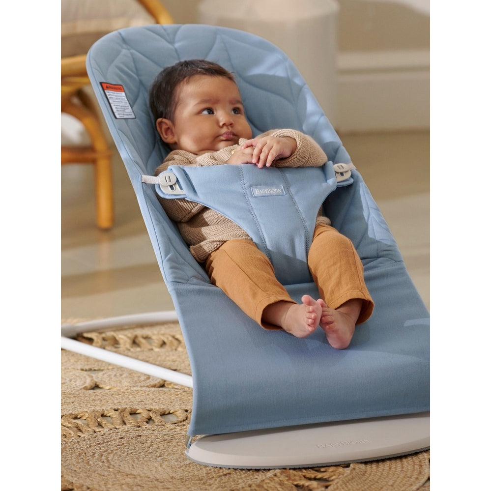 BabyBjörn Bouncer Bliss in blue, where a baby sits securely with harness, calmly lounging.