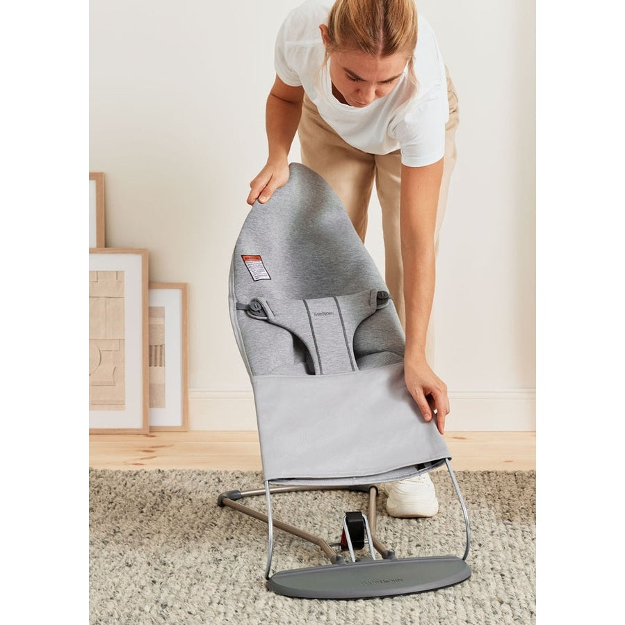 BabyBjörn Bouncer Bliss in gray fabric with a metal frame being unfolded by a parent for quick setup.