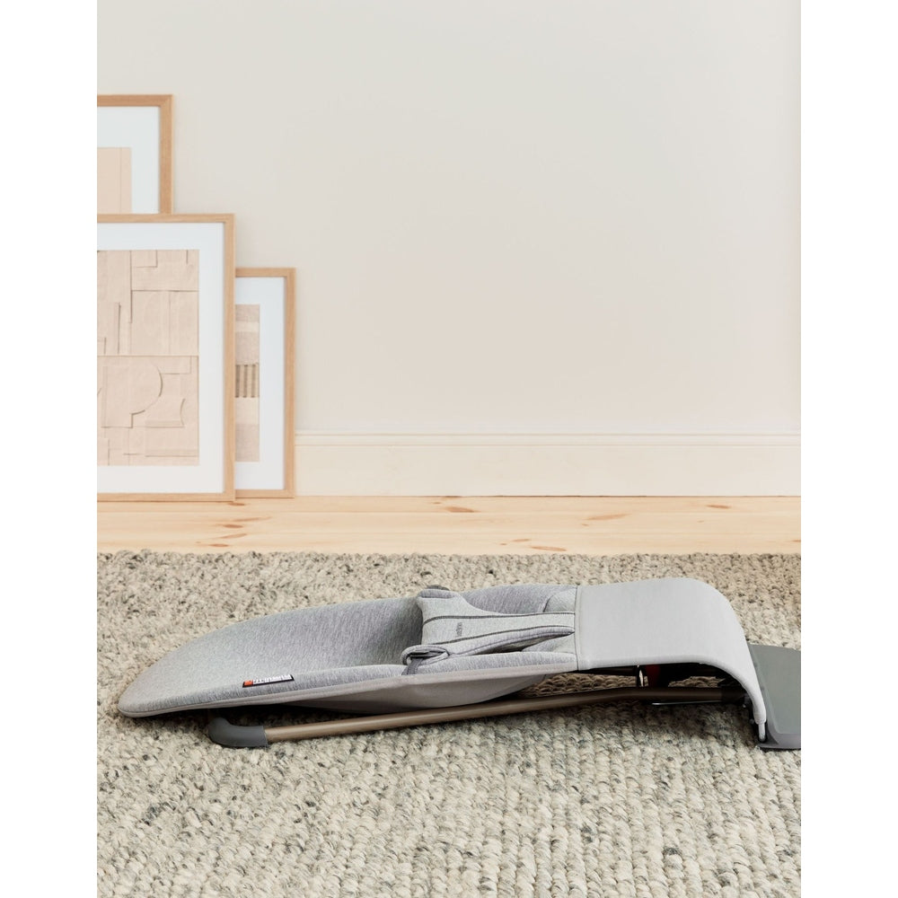 BabyBjörn Bouncer Bliss in light gray folded compactly on a textured rug, showing easy storage.
