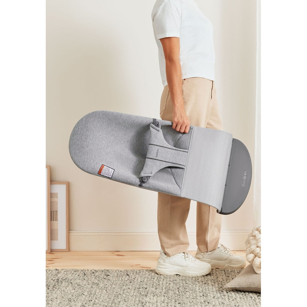 BABYBJÖRN Bouncer Bliss in gray, being carried by a person to show its compact fold for easy transport.