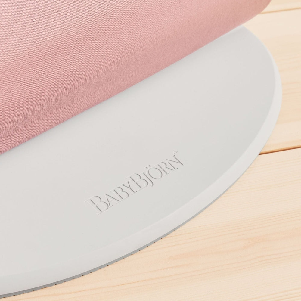BabyBjörn Bouncer Bliss in pink fabric resting on a gray curved base, showcasing a soft, supportive seat.