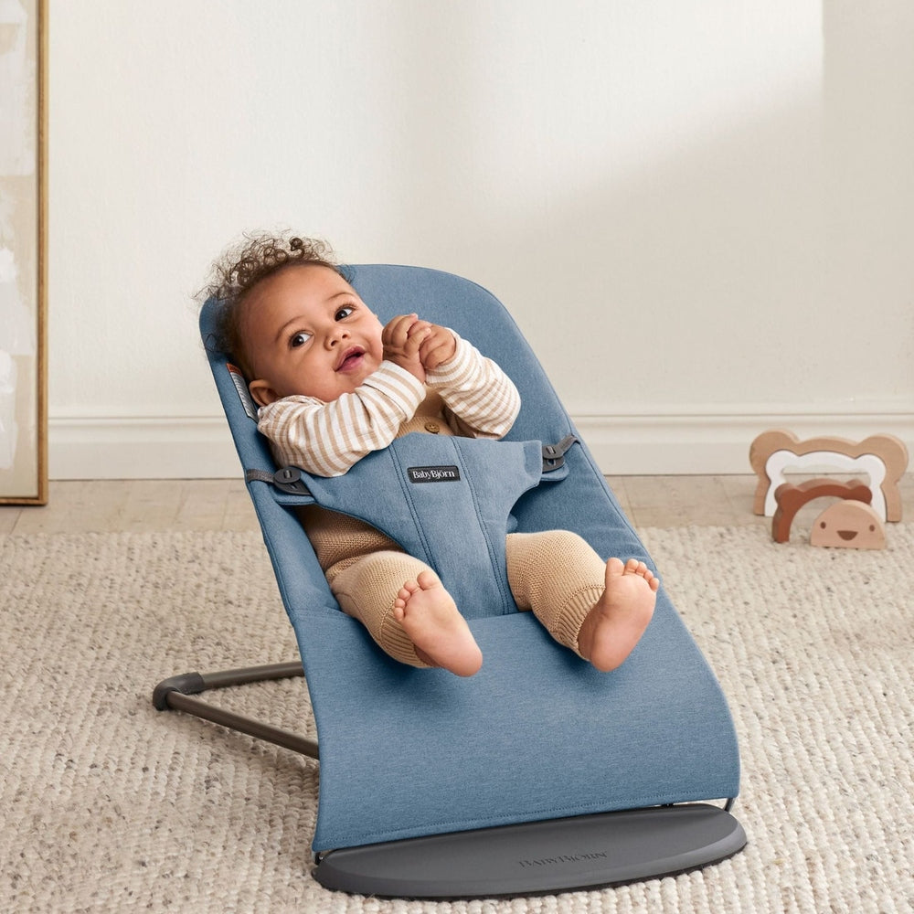 BabyBjörn Bouncer Bliss in blue fabric, a baby calmly reclines in the rocker on a gray base.