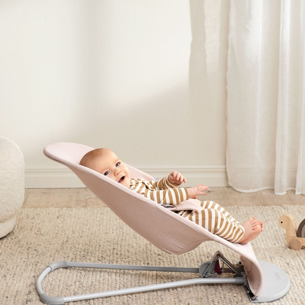 BabyBjörn Bouncer Bliss pink fabric seat with gray frame; baby reclines calmly.