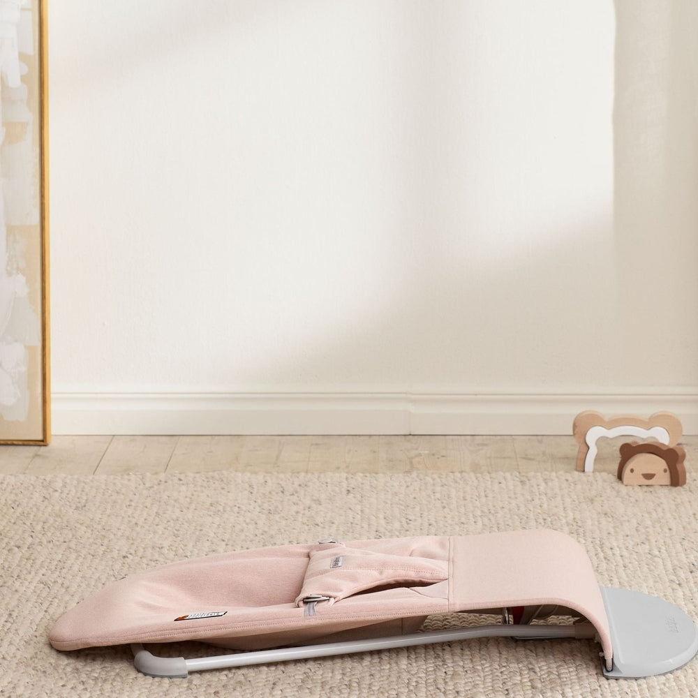 BabyBjörn Bouncer Bliss pink folded for compact storage, showing a lightweight gray frame on a beige rug.
