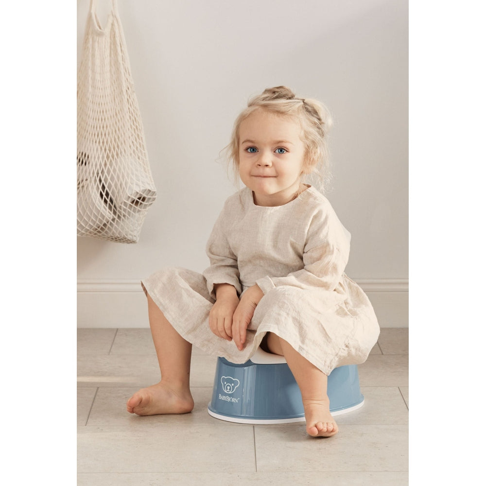 BabyBjörn Smart Potty in blue, a toddler sits on it calmly during potty training, feet on the floor.