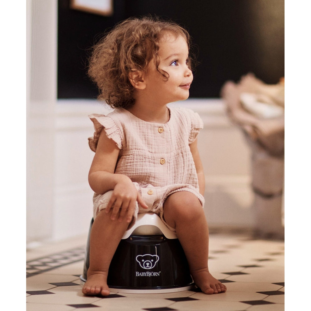 BabyBjörn Smart Potty, black base with white seat; toddler sits securely, showing compact ergonomic design.