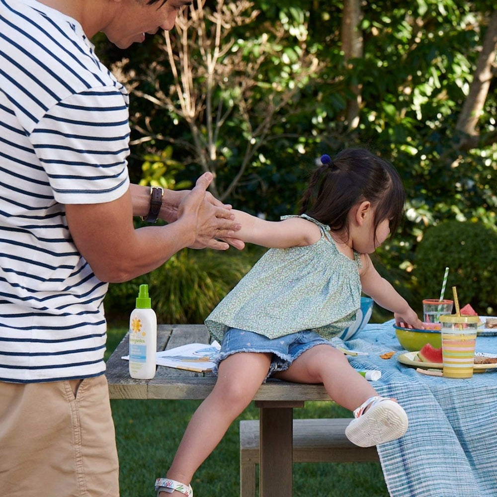 Babyganics Mineral Sunscreen Spray SPF50, 6 oz bottle on a picnic table outdoors with a child.
